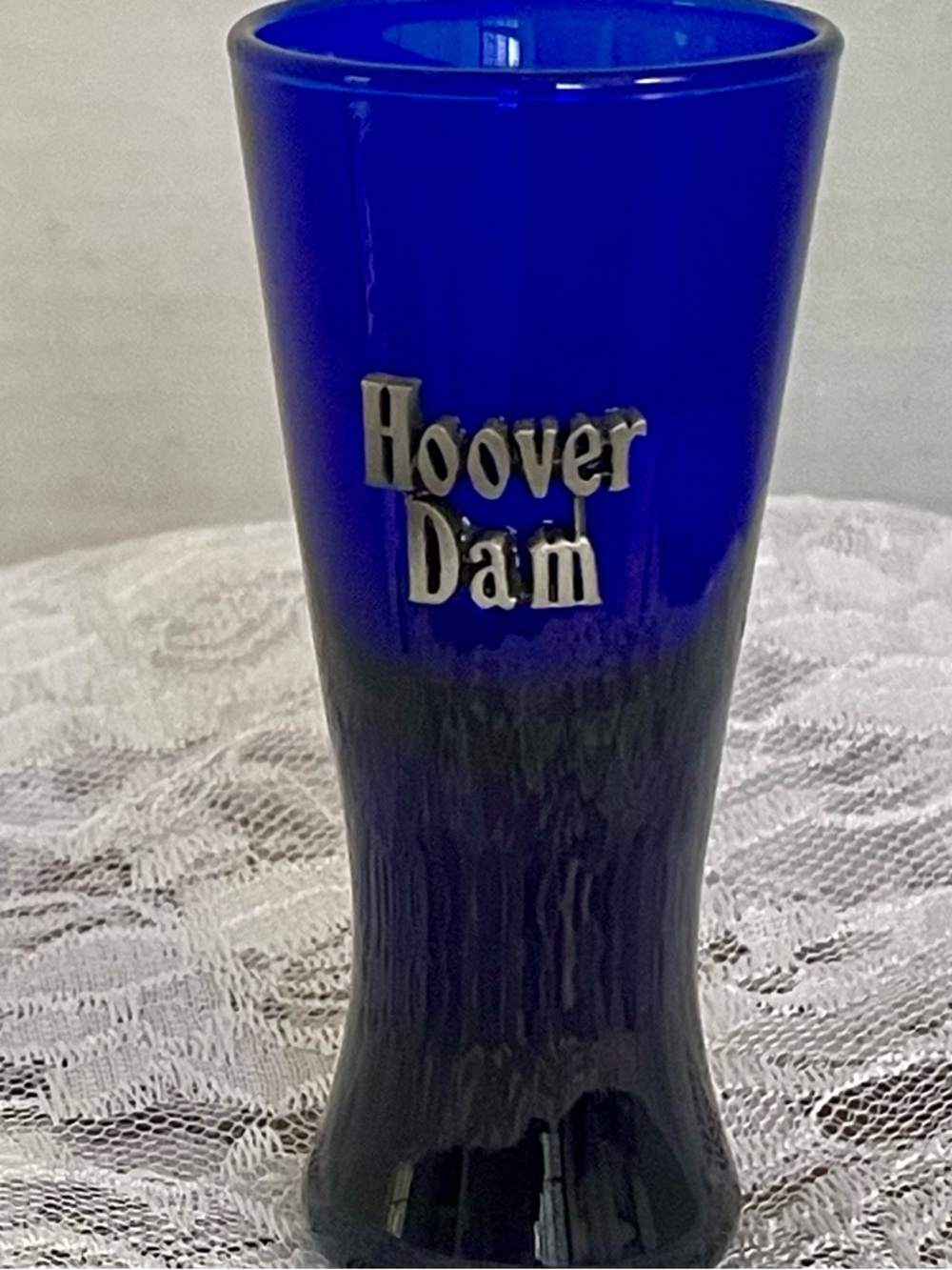 A cobalt blue glass shot glass featuring pewter emblem that reads "Hoover Dam".